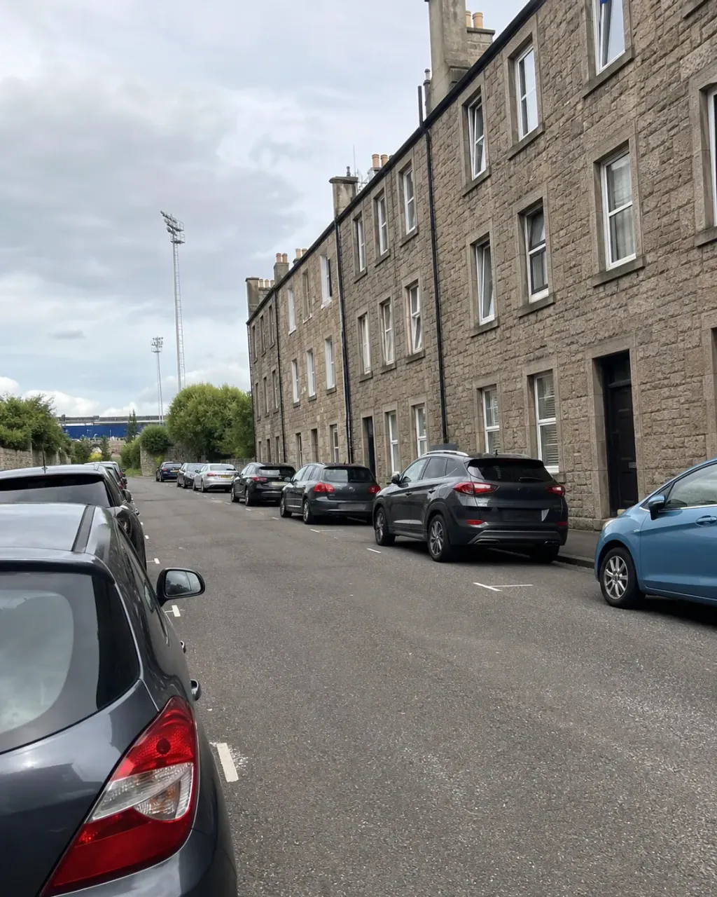 Stone tenements and parked cars on a Gorgie side street, floodlights beyond